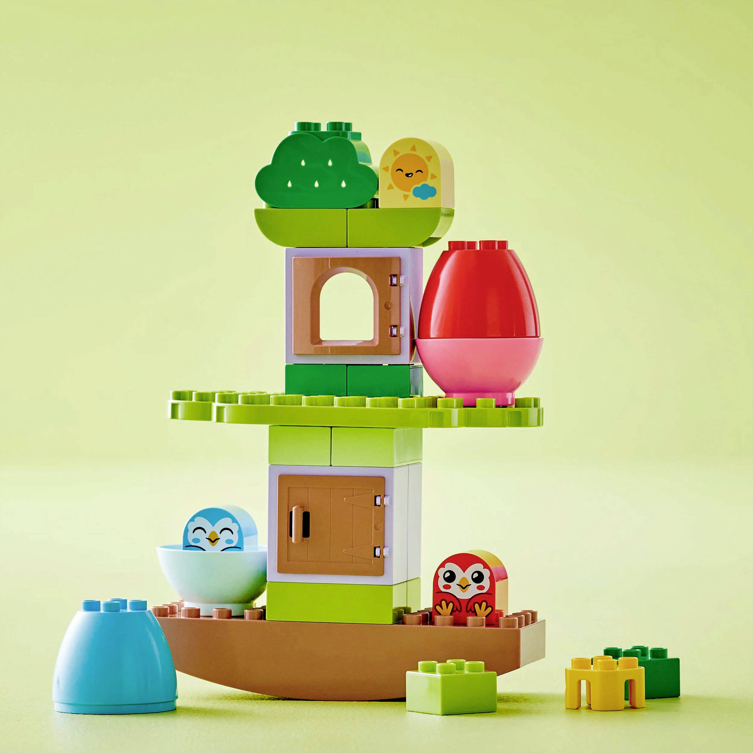 A colourful tower made of LEGO-Duplo bricks with figures and doors, built in cheerful colours on a light green background.