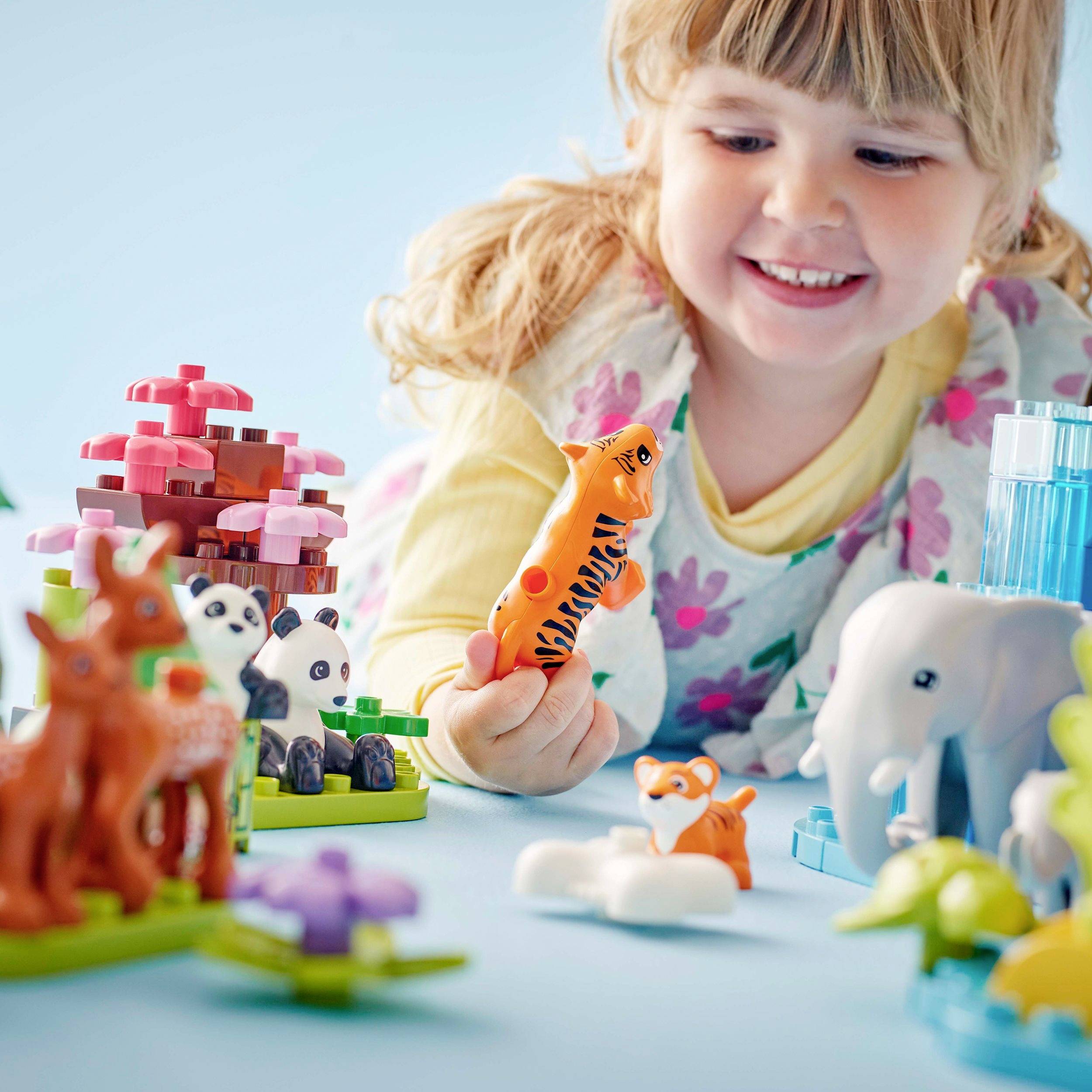 A child happily plays with colourful animal figurines and building blocks on a table. The focus is on the child's interaction and creativity.