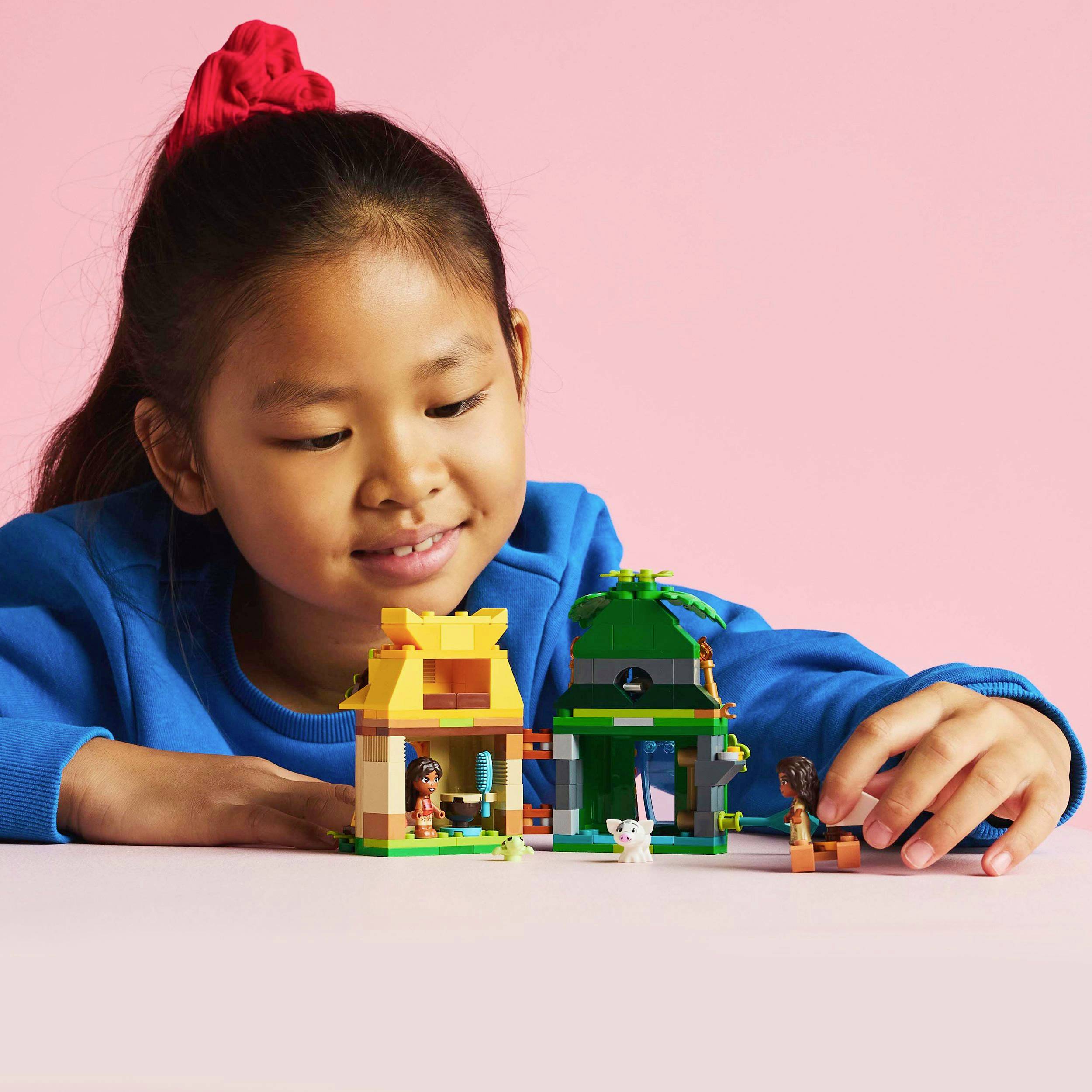 A child builds with colourful Lego bricks, smiles and looks concentrated. In the foreground, small, assembled structures can be seen.