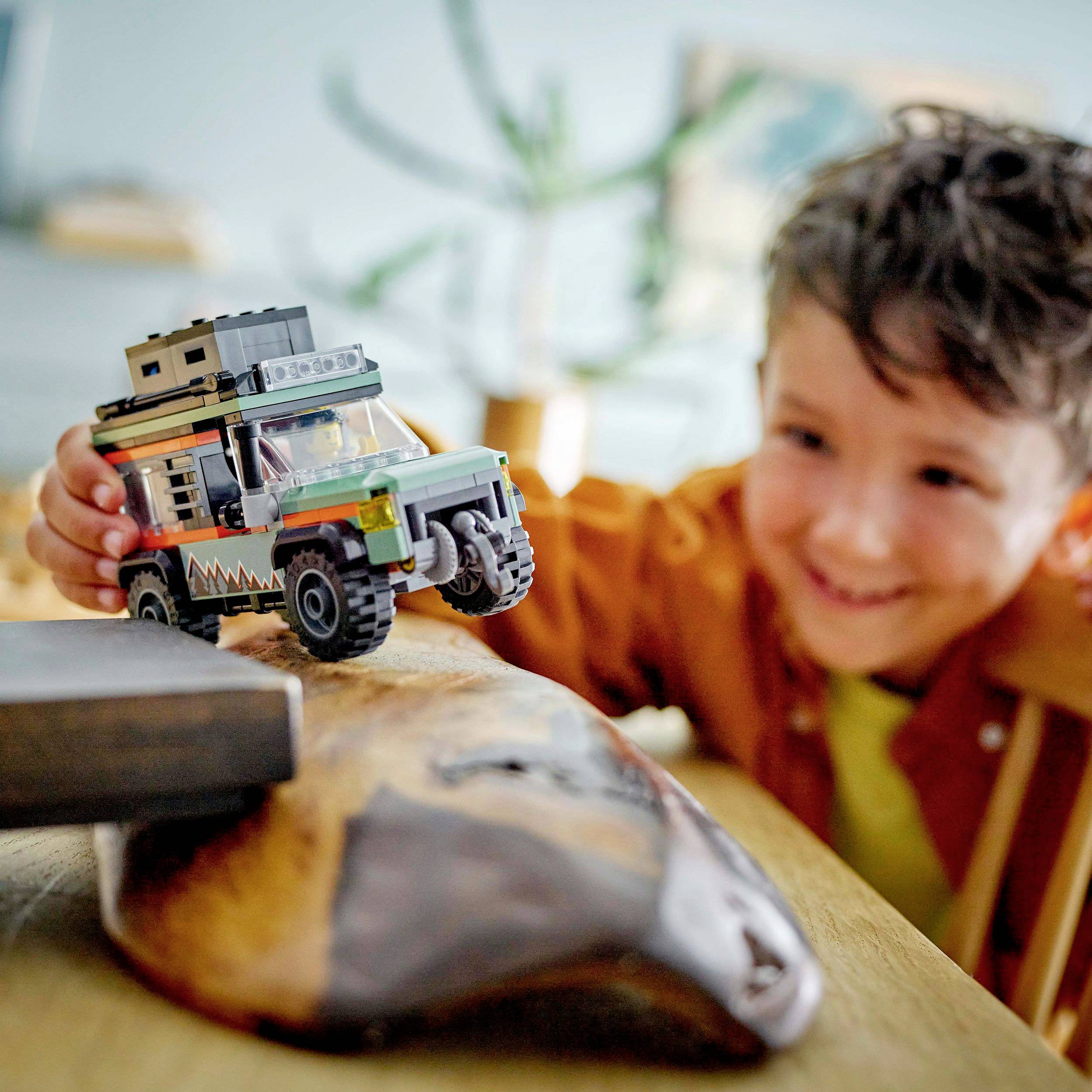 A child is happily playing with a toy car on a table. The car has a coloured roof and off-road tyres.