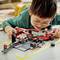 A child is playing on the floor with a racing track Lego set, carefully assembling a small red car.