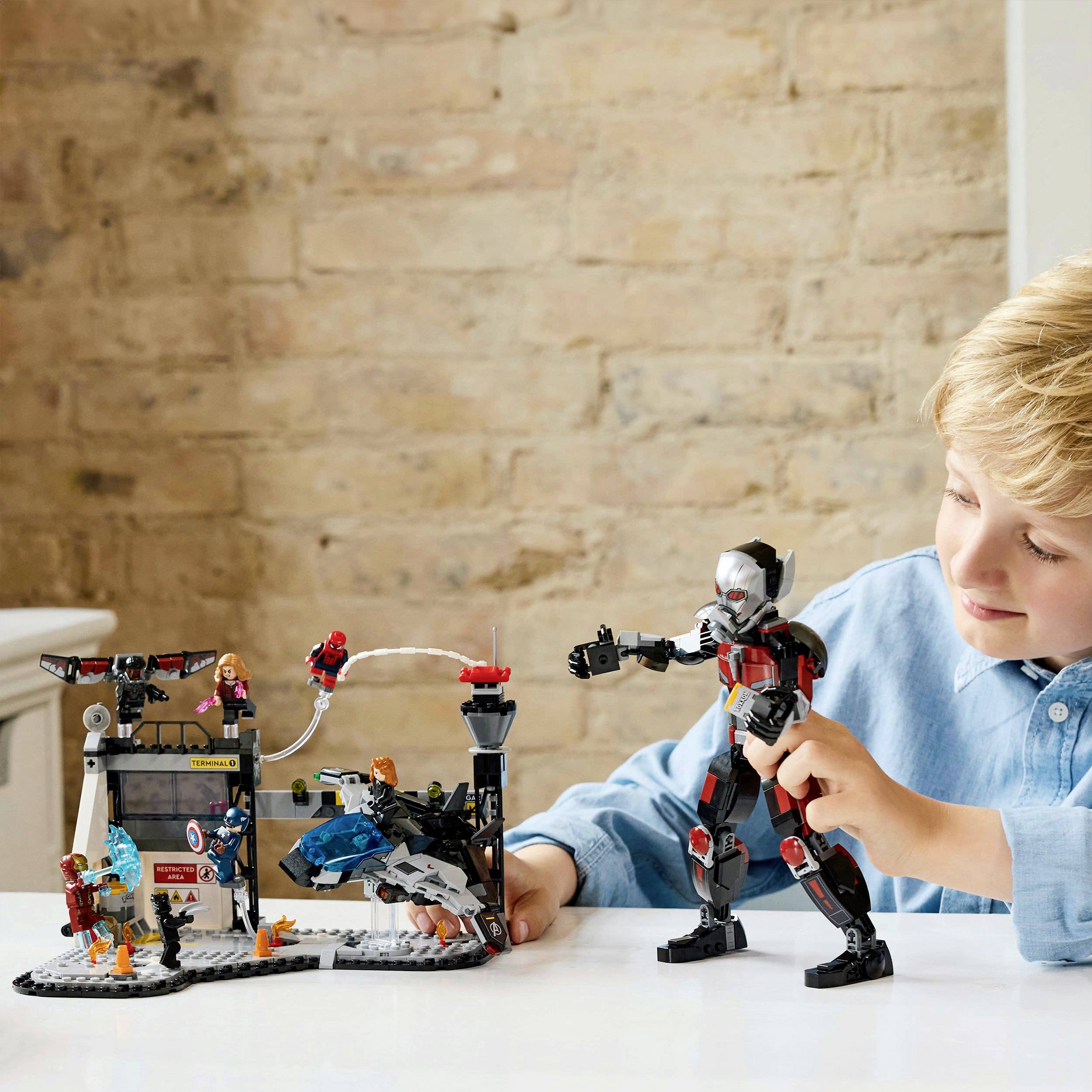 A child is playing with building blocks and figurines on a table in front of a brick wall. The child is deeply absorbed in the game.