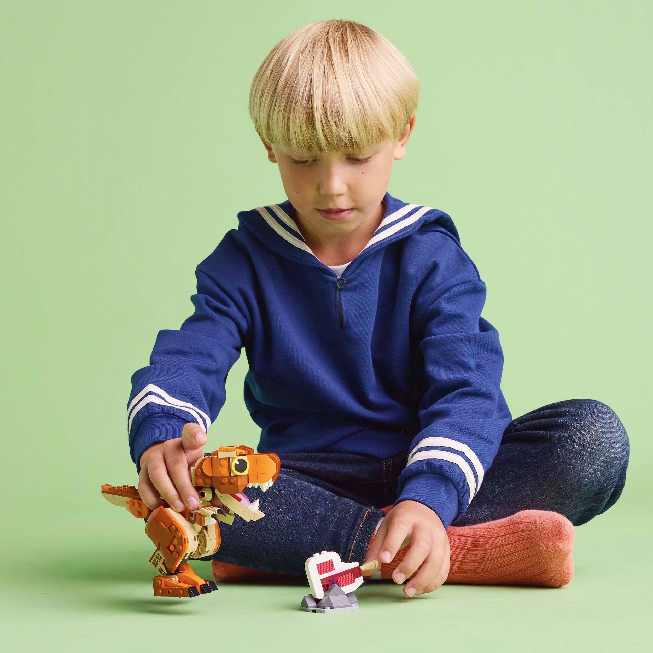 A child in a blue jumper is playing with a small orange robot toy on a green background.