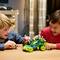 Two children are playing with a remote-controlled car on a table. The car is colourful and has large wheels. Both children are smiling.