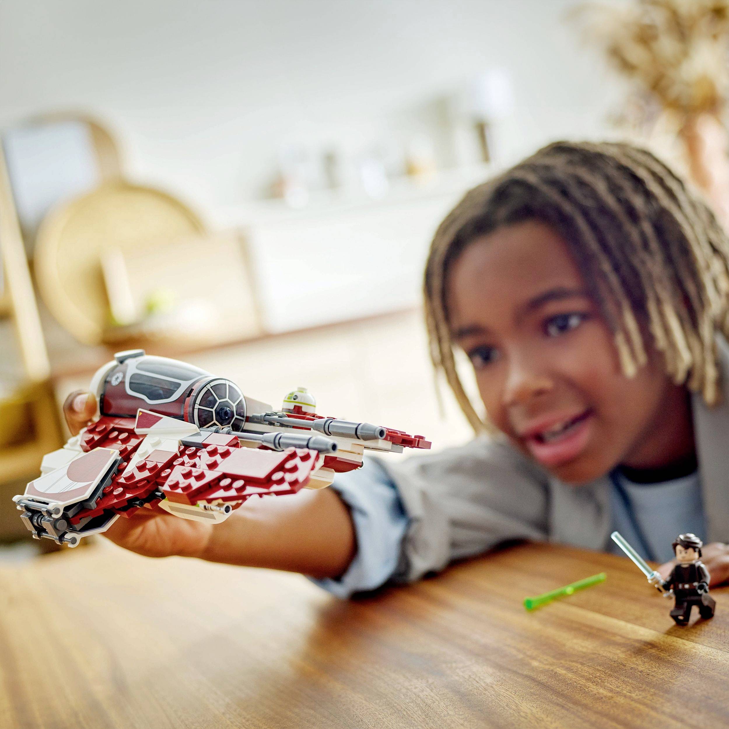 A child is playing with a model spacecraft on a table. The child appears focused and is holding the toy carefully in their hands.