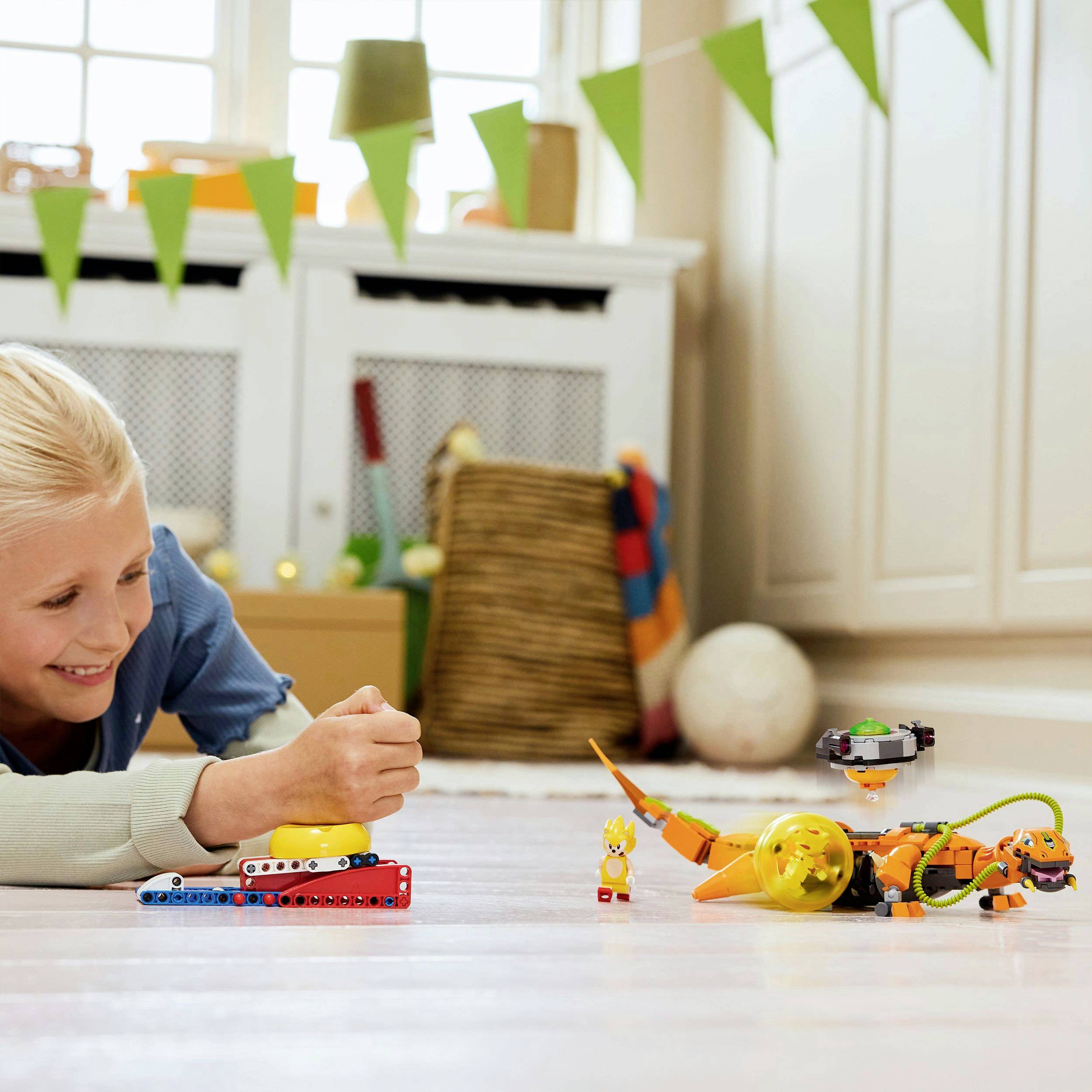A child is happily playing on the floor with colourful toys and robots in a bright room with decorations and a basket in the background.