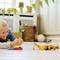 A child is happily playing on the floor with colourful toys and robots in a bright room with decorations and a basket in the background.