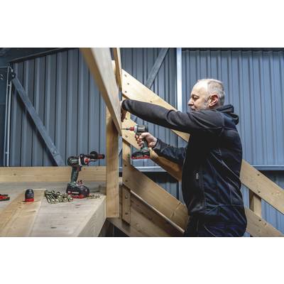 A man is working with a drill on a wooden structure. Additional tools and screws are laid out on the table.