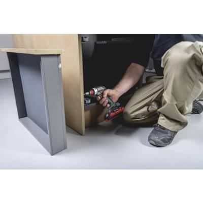 A person is fixing cabinets with a cordless drill. They are wearing work clothes and focusing intently on the piece of furniture.