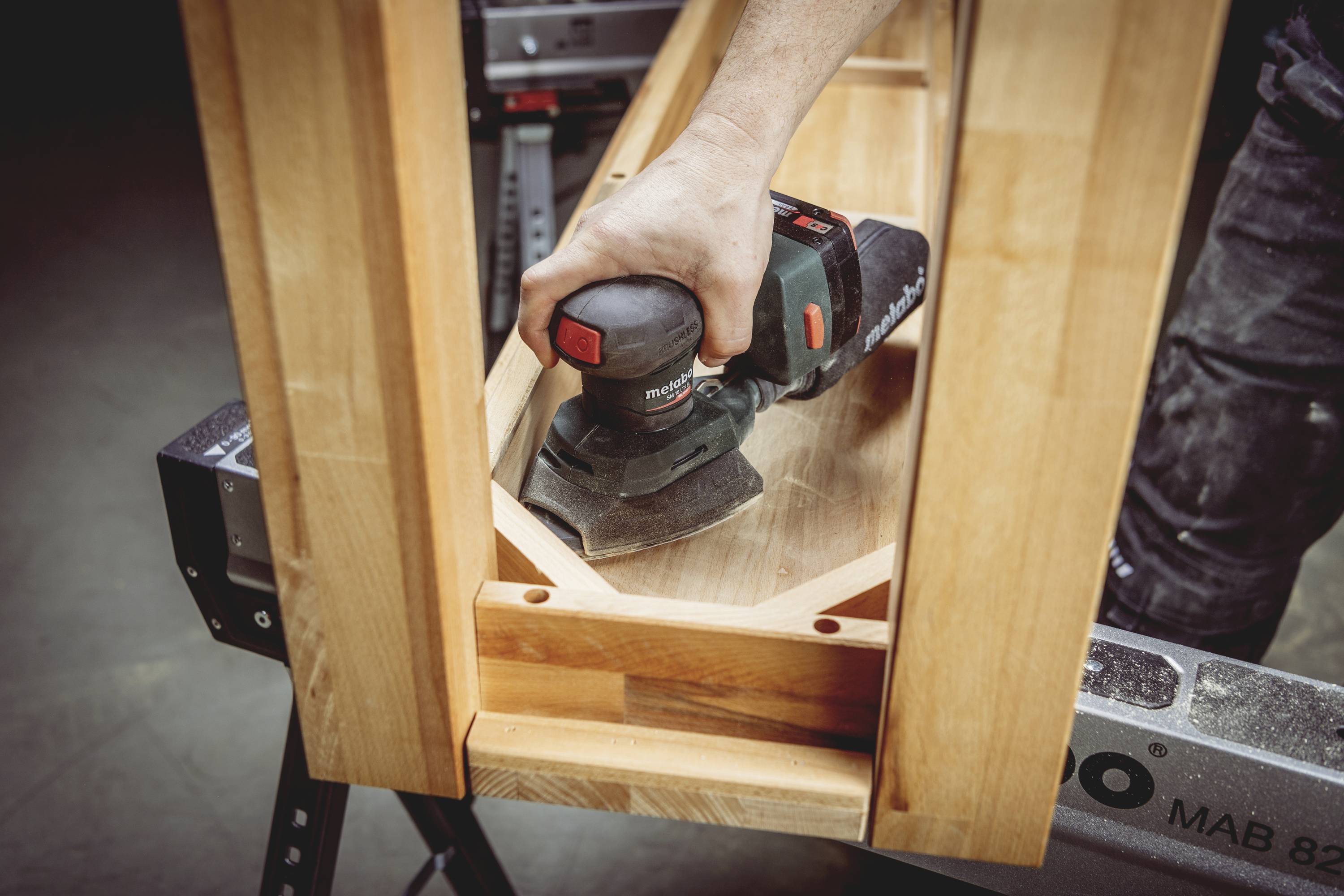 A person is sanding the surface of a wooden piece of furniture, most likely a table or shelf, using an electric sander.