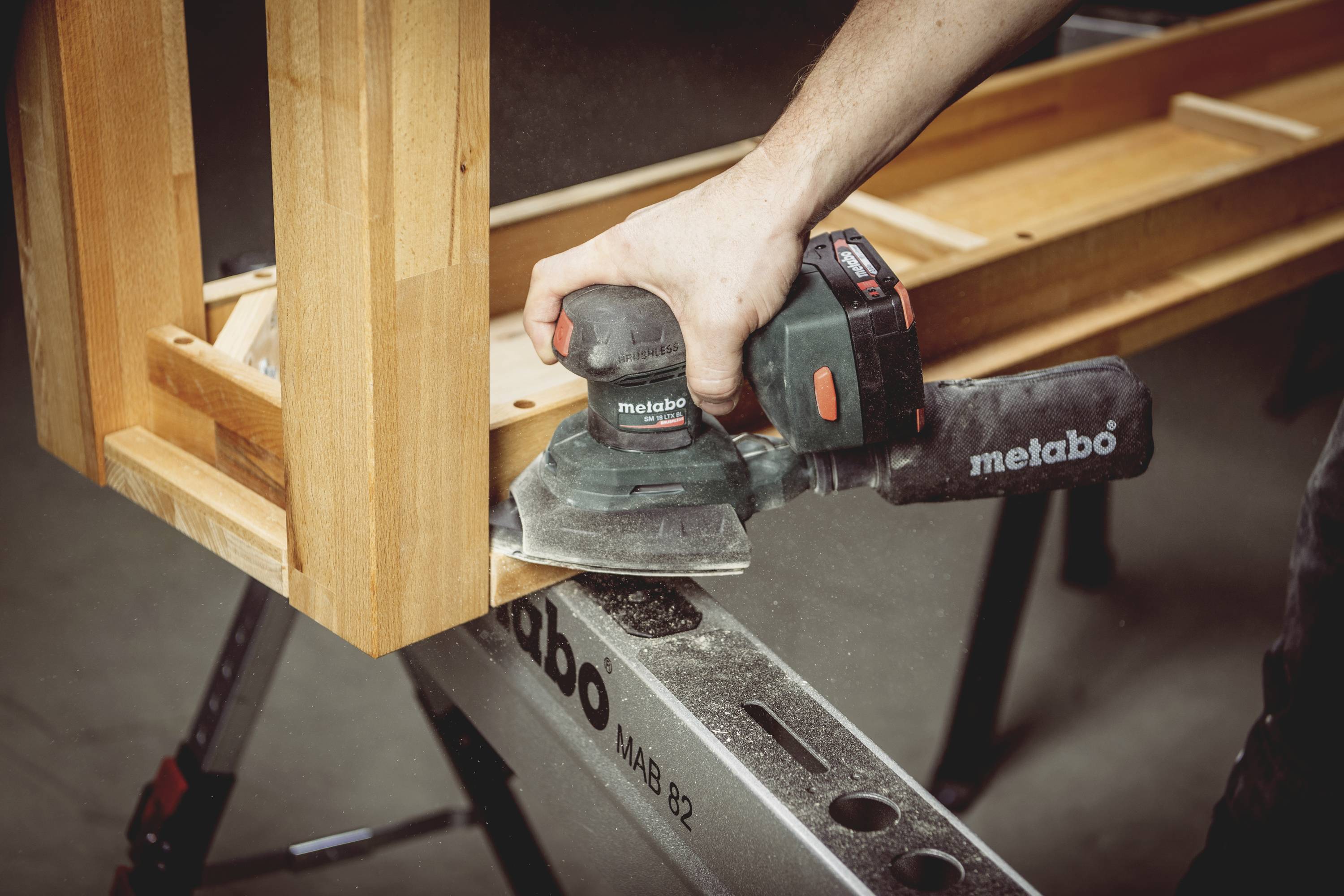 A person is sanding wood with a Metabo tool. The table is being worked on to create a smooth surface.