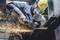 A worker in protective clothing grinds metal with a grinding machine, sparks flying.