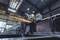 A worker wearing a hard hat is grinding metal in an industrial workshop. Sparks are flying as he works on a large piece of metalwork.