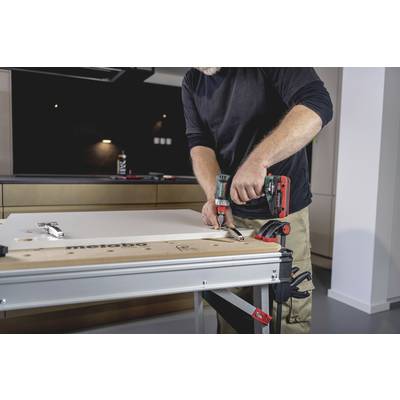 A person is attaching a hinge to a white board with a cordless drill in a workshop environment.