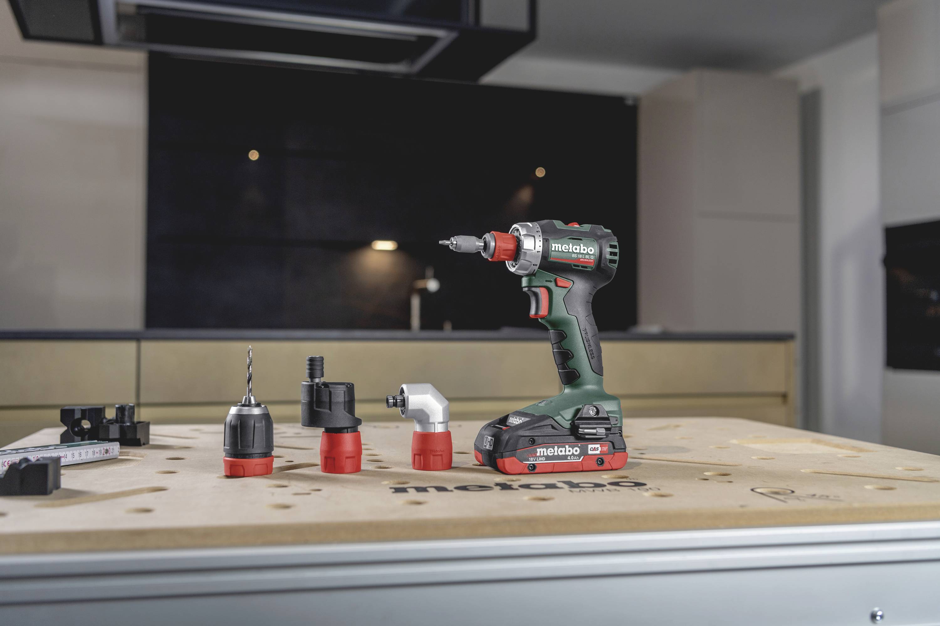 Cordless drill with multiple attachments on a table in a modern kitchen.
