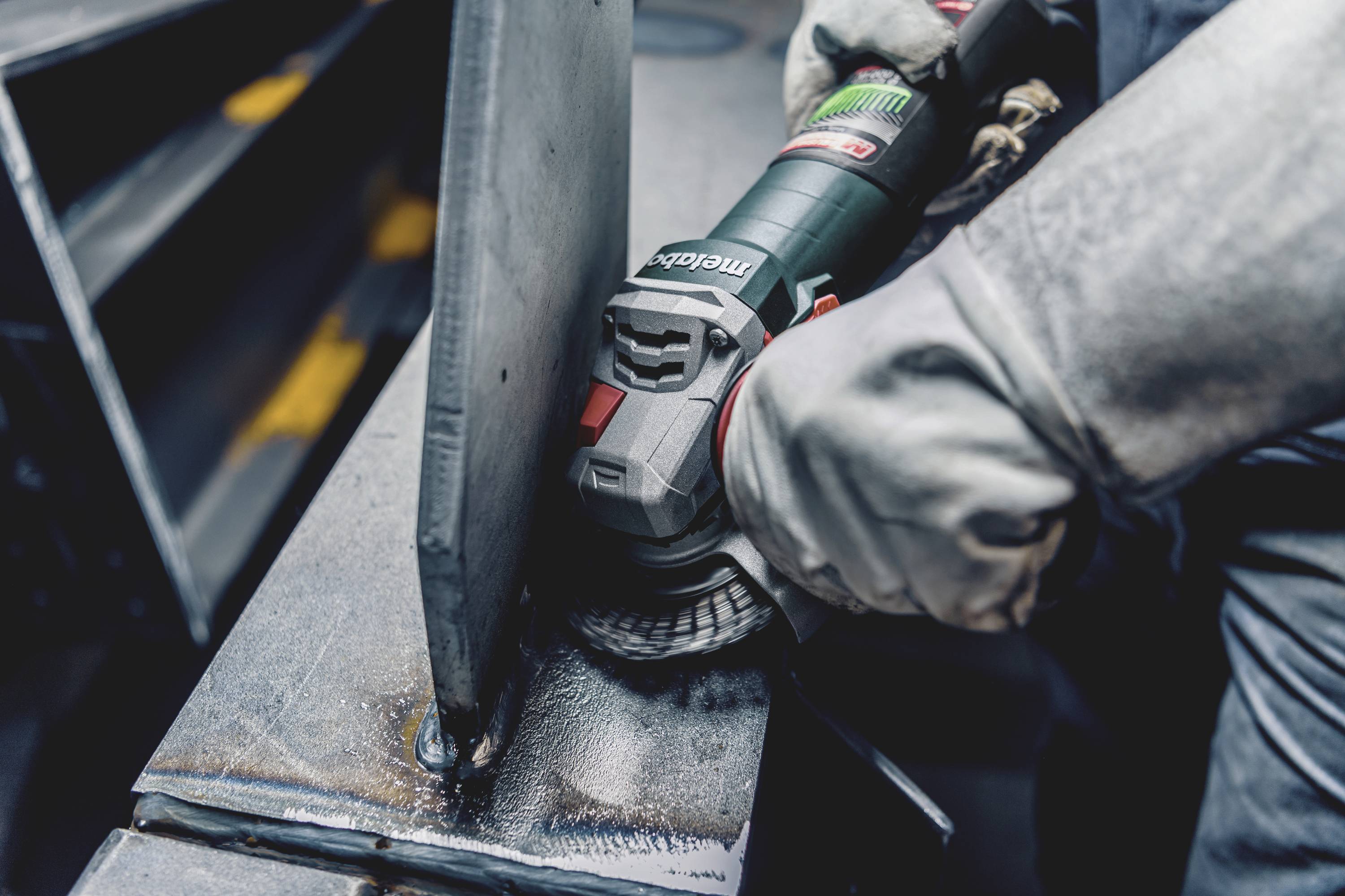A person is working on a metal plate with an angle grinder. Sparks and metal shavings are visible. Protective clothing is being worn.