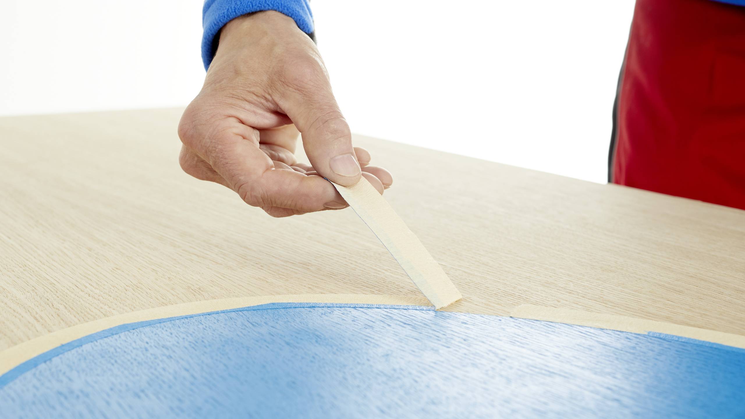 A hand is drawing a wooden edge along a blue table covering. The table is light brown.