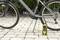 A black bicycle on cobblestones stands next to a yellow portable bicycle pump. The bicycle is unused and the pump is ready.