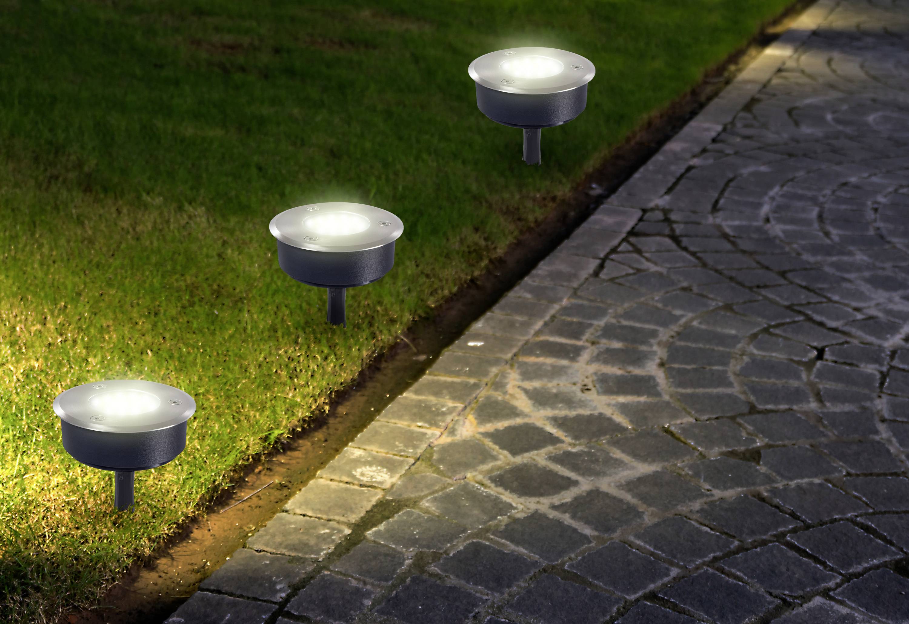 Solar pathway lights illuminating a grassy area beside a paved walkway at night.