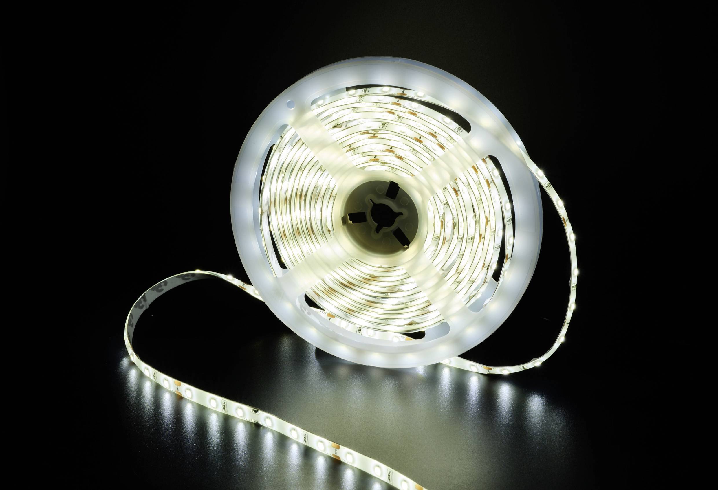 A roll of LED light strip, partially unrolled, illuminates against a black background. The LEDs emit a cold, white light.