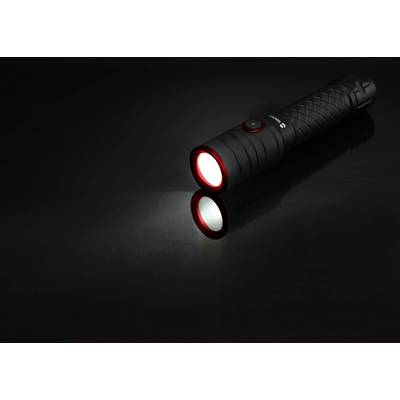 A black torch lying on a shiny surface, shining a white beam forwards.