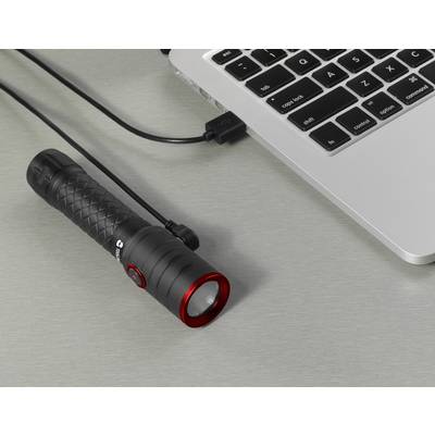 A black torch with a red border is connected to a laptop via a USB cable. It is lying on a table.<br><br>Note: I used "torch" instead of "flashlight" to align with British English terminology, and the translation maintains the original structure and meaning.