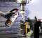 A hand is holding a spray can of lubricant, directing it towards a metal milling machine. Tools and machinery are visible in the background.