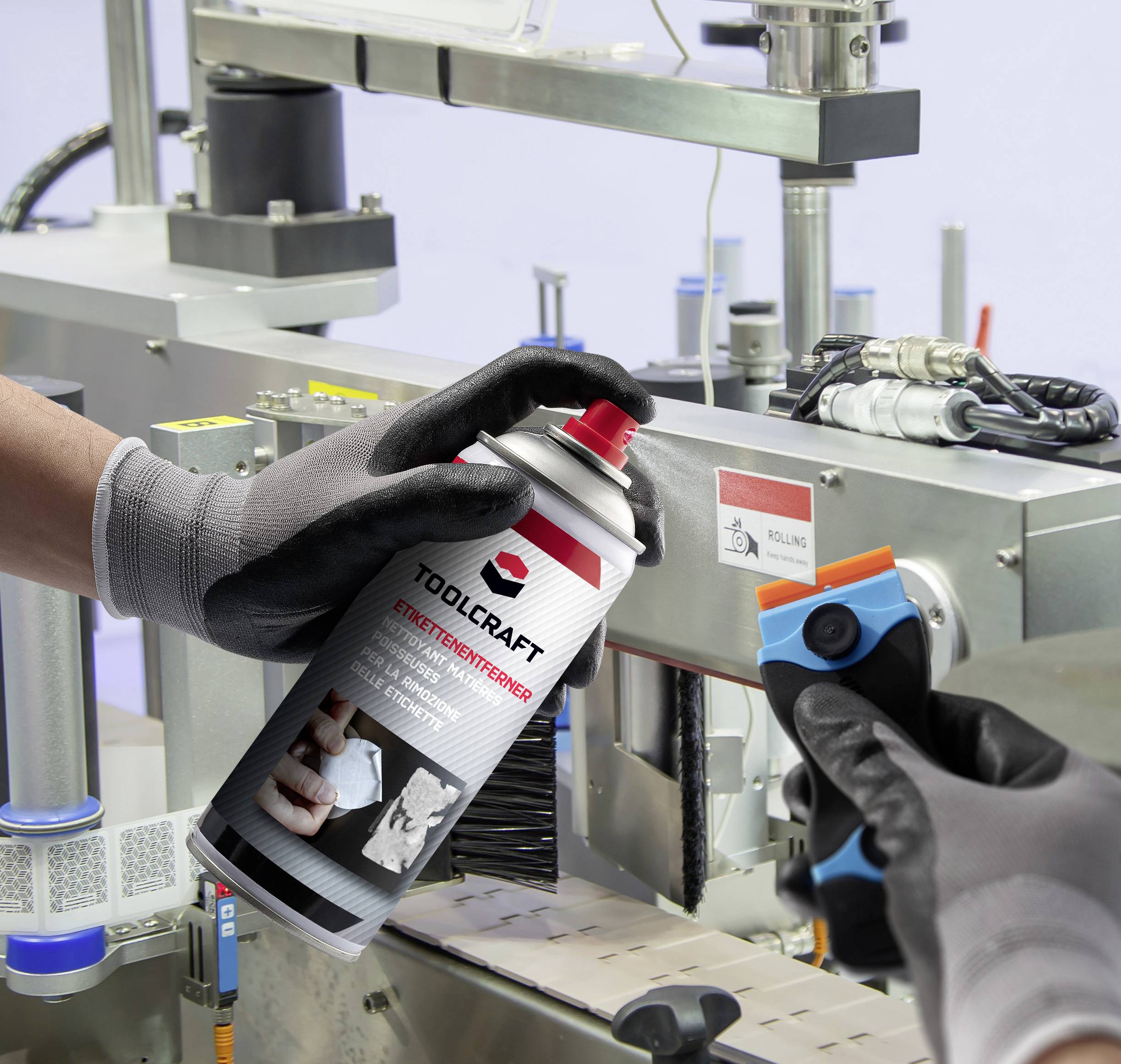 A person wearing gloves is spraying tool protection spray onto a machine while holding a scraper.