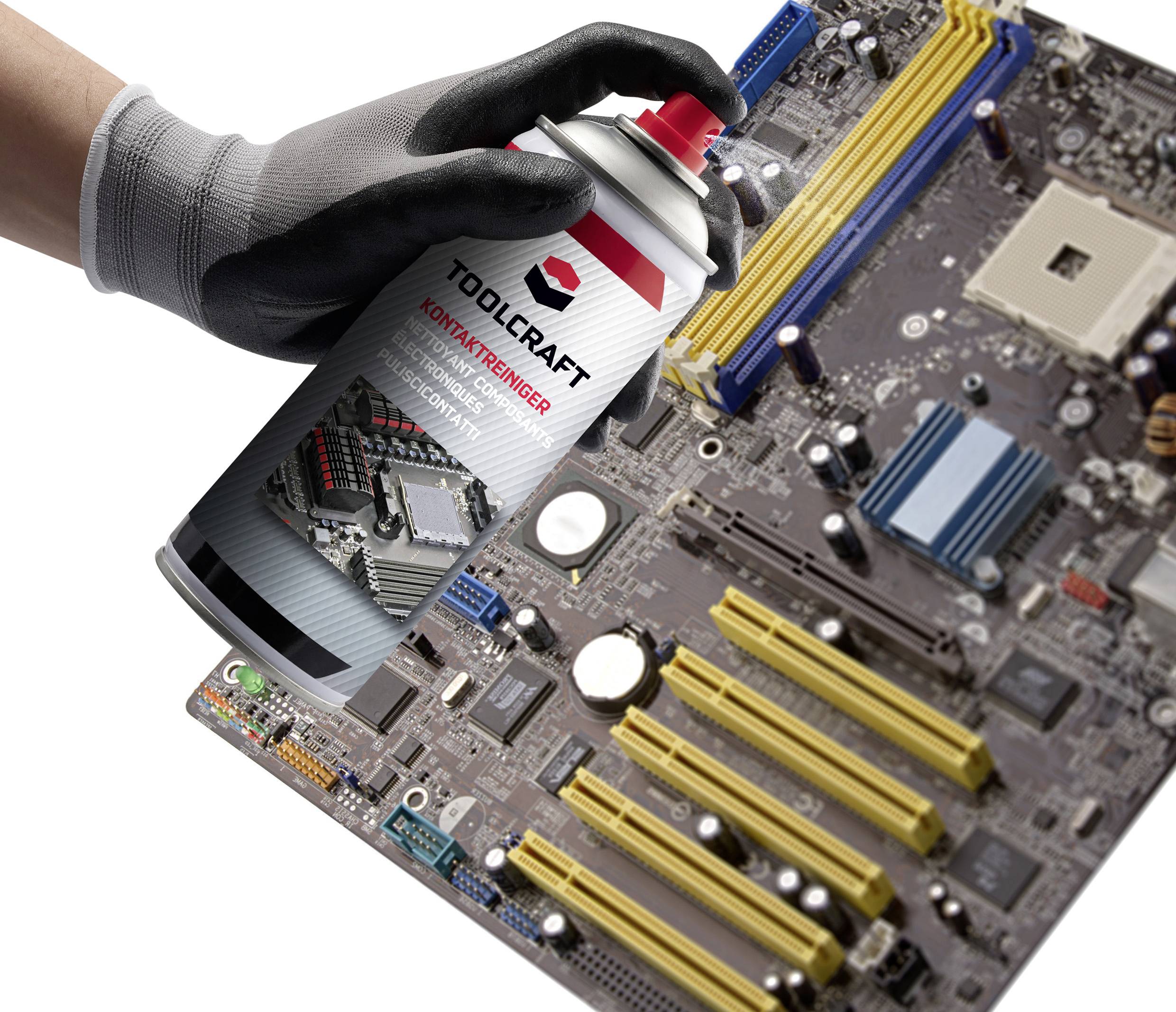 A hand in a glove holds a Toolcraft spray can over a computer motherboard to clean it.