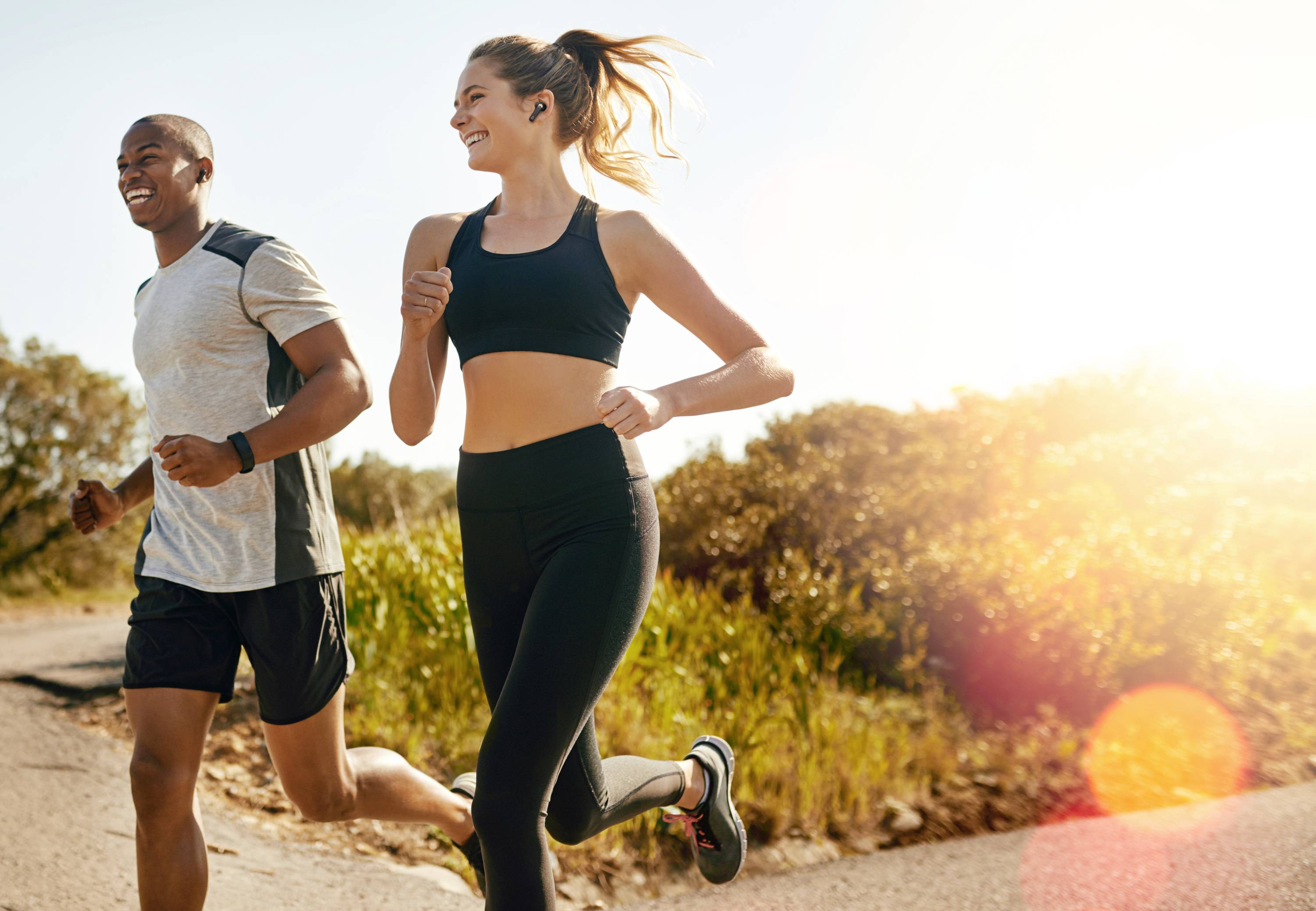 Two people are jogging cheerfully in sunny weather along a country path, surrounded by lush greenery.