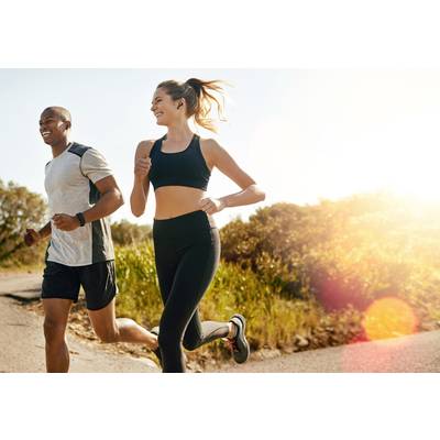 Two people are jogging cheerfully in sunny weather along a country path, surrounded by lush greenery.