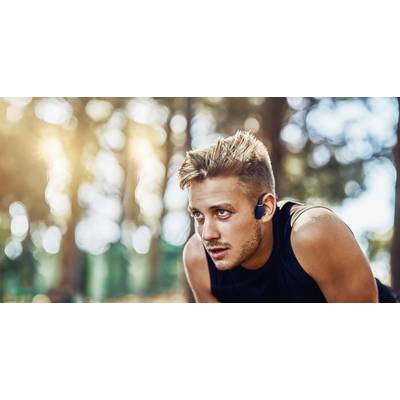 A young man with headphones is preparing for a run. He gazes intently into the distance. Trees are visible in the background.