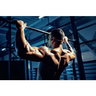 A muscular man is doing pull-ups in a fitness studio. The environment is dark, with blue lighting that accentuates the room.