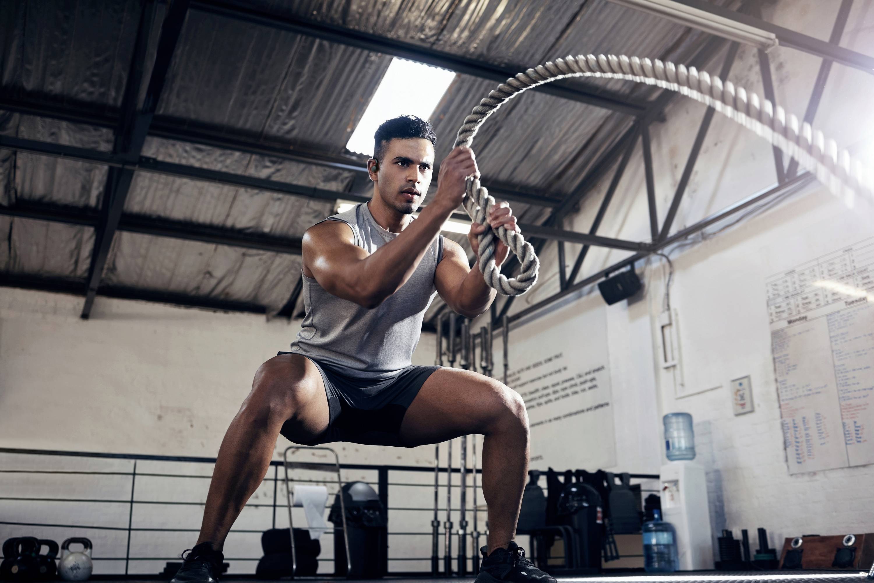 A man is training with battle ropes in a gym. He is wearing sportswear and is in a powerful pose.