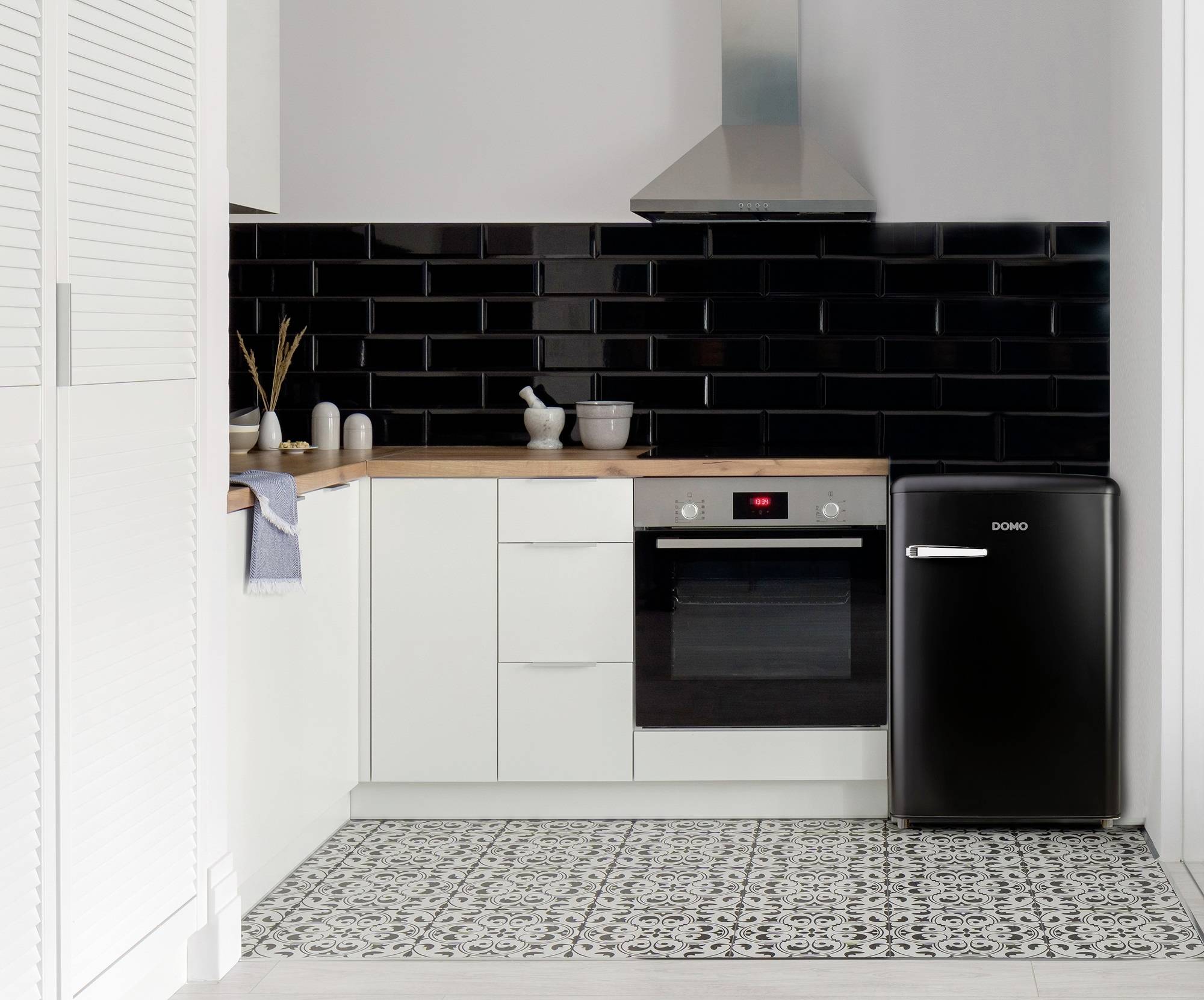 Modern kitchen with white furnishings, black splashback and small black fridge. Surfaces are clean and tidy.