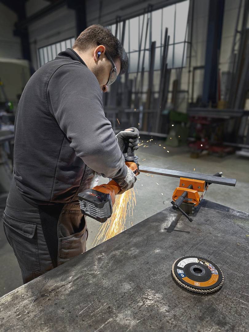 A man in a workshop is cutting a piece of metal with an angle grinder. Sparks are flying in all directions.