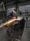 A person is grinding a metal piece with an angle grinder, sparks flying. In the background, a workshop hall.