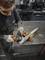 A person is grinding metal with a grinding machine on a table. They are wearing safety glasses and gloves for protection.
