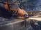 A person is grinding a metal piece with an angle grinder, sparks flying. The scene is set in a workshop.