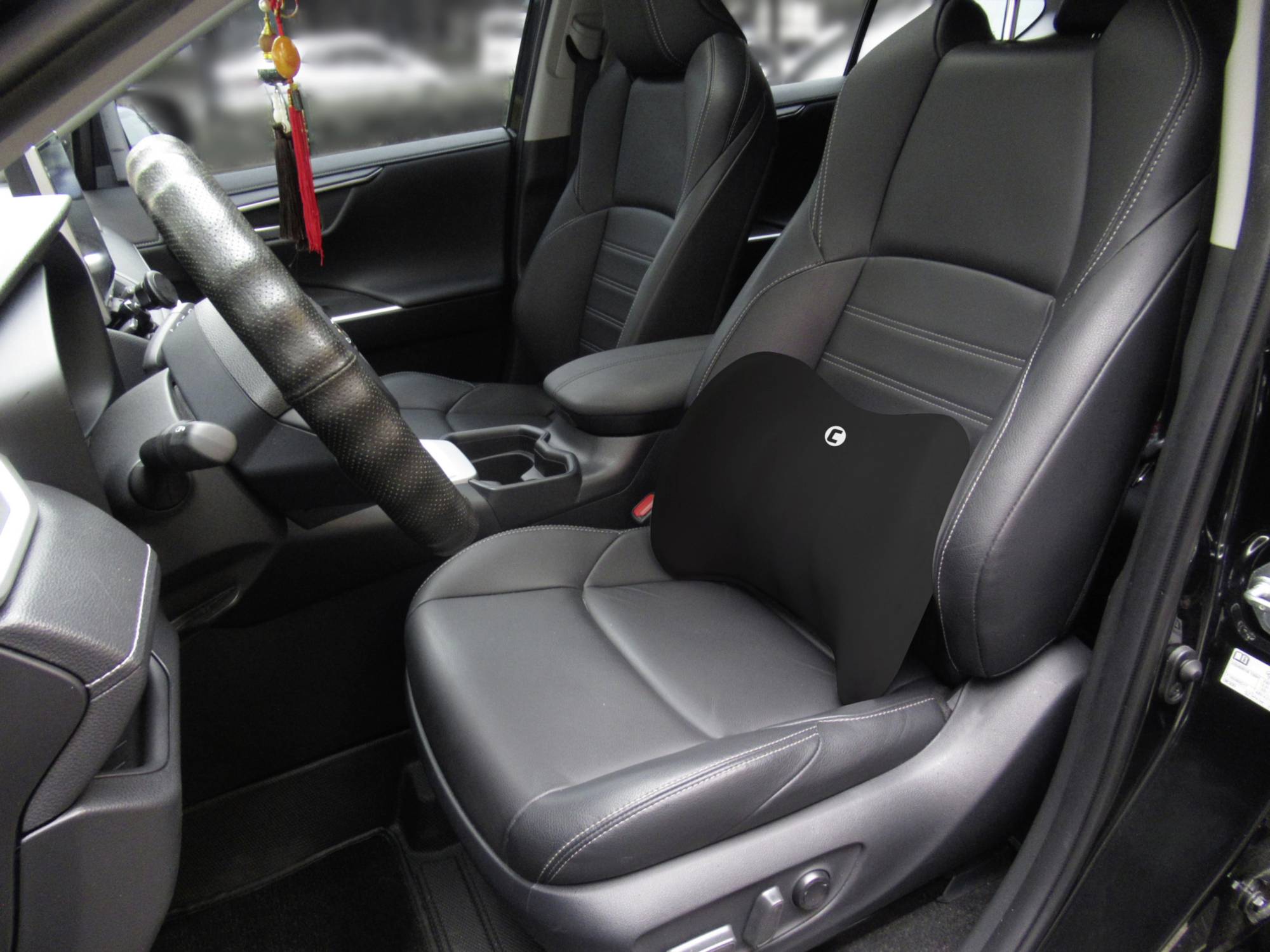 'Interior of a car: passenger seat with a black lumbar cushion on it. Steering wheel, dashboard and car doors are visible.'