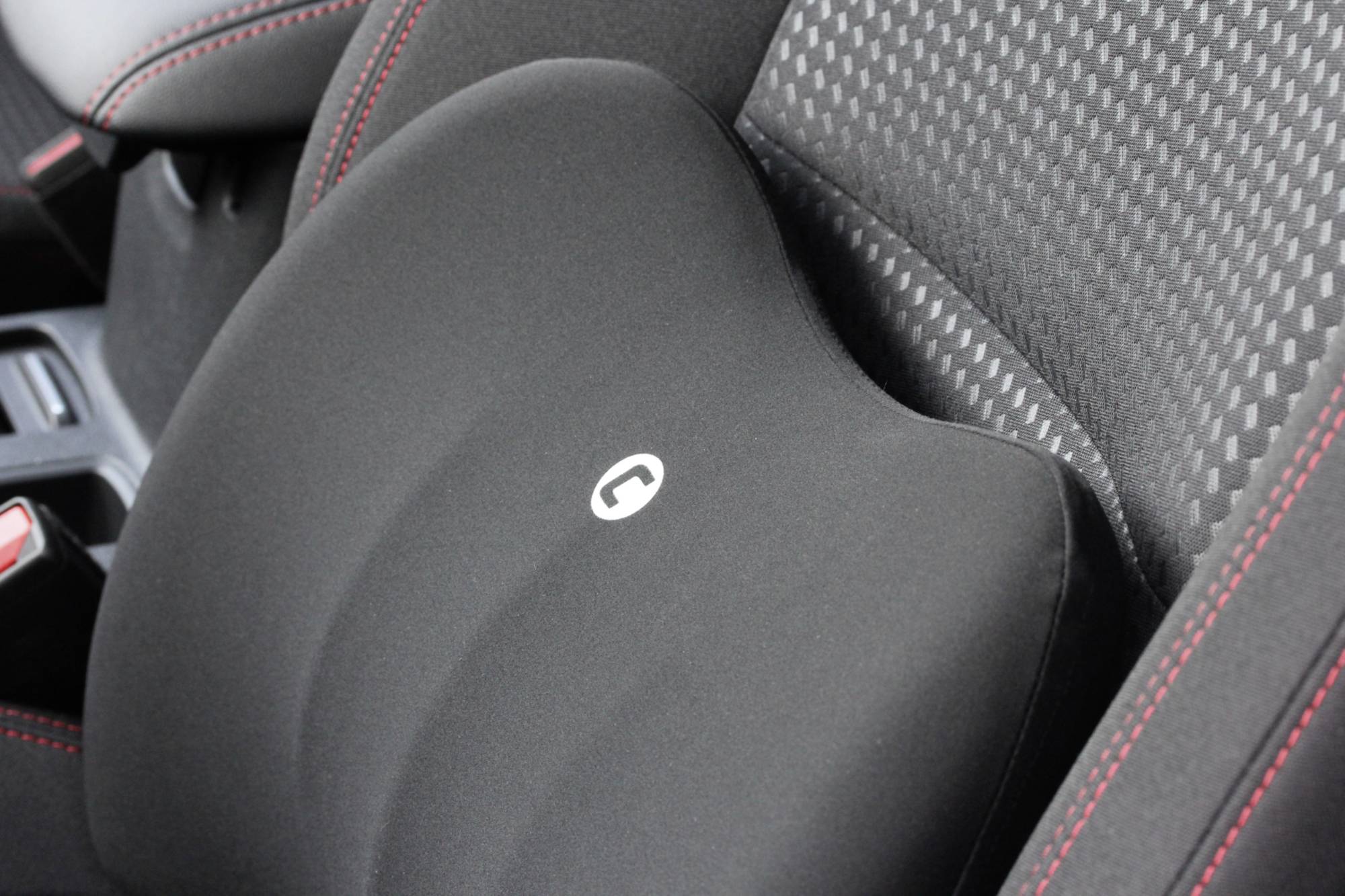 A black lumbar cushion on a car seat with red stitching provides additional comfort and support while driving.