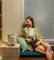 A woman is sitting on a window ledge beside a projector, holding a remote control. The scene feels cosy and relaxed.