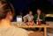 A projector displays an image in a nighttime outdoor scene. Two people are seated, with drinks and snacks on a table.