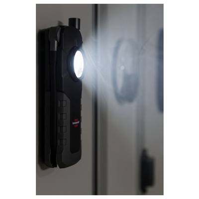 A wall-mounted black charging station or device with a bright circular light, viewed in close-up beside a reflective surface.