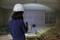 A person wearing a hard hat and carrying a torch inspects a construction site with pallets in a semi-finished concrete structure.