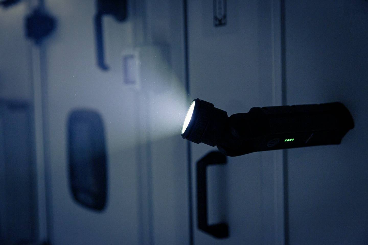 'A torch illuminates a dark room and lights up a wall with handles that could be in a vehicle or technical area.'