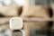 A small, square, cream-coloured device with a circular pattern rests on a smooth surface, with a blurred background.