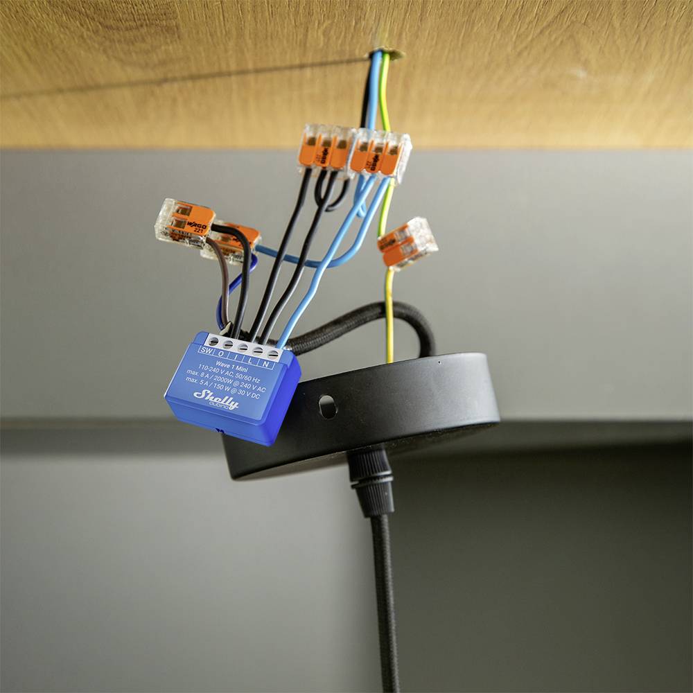 A smart switch is being installed on several coloured cables beneath a ceiling plate.