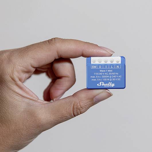 A hand is holding a small, blue electronic device with the inscription 'V1 Mini'. The device displays voltage and power specifications.
