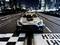 A model racing car with the inscription 'Safety Car' drives on an illuminated racetrack in front of a blurred cityscape.